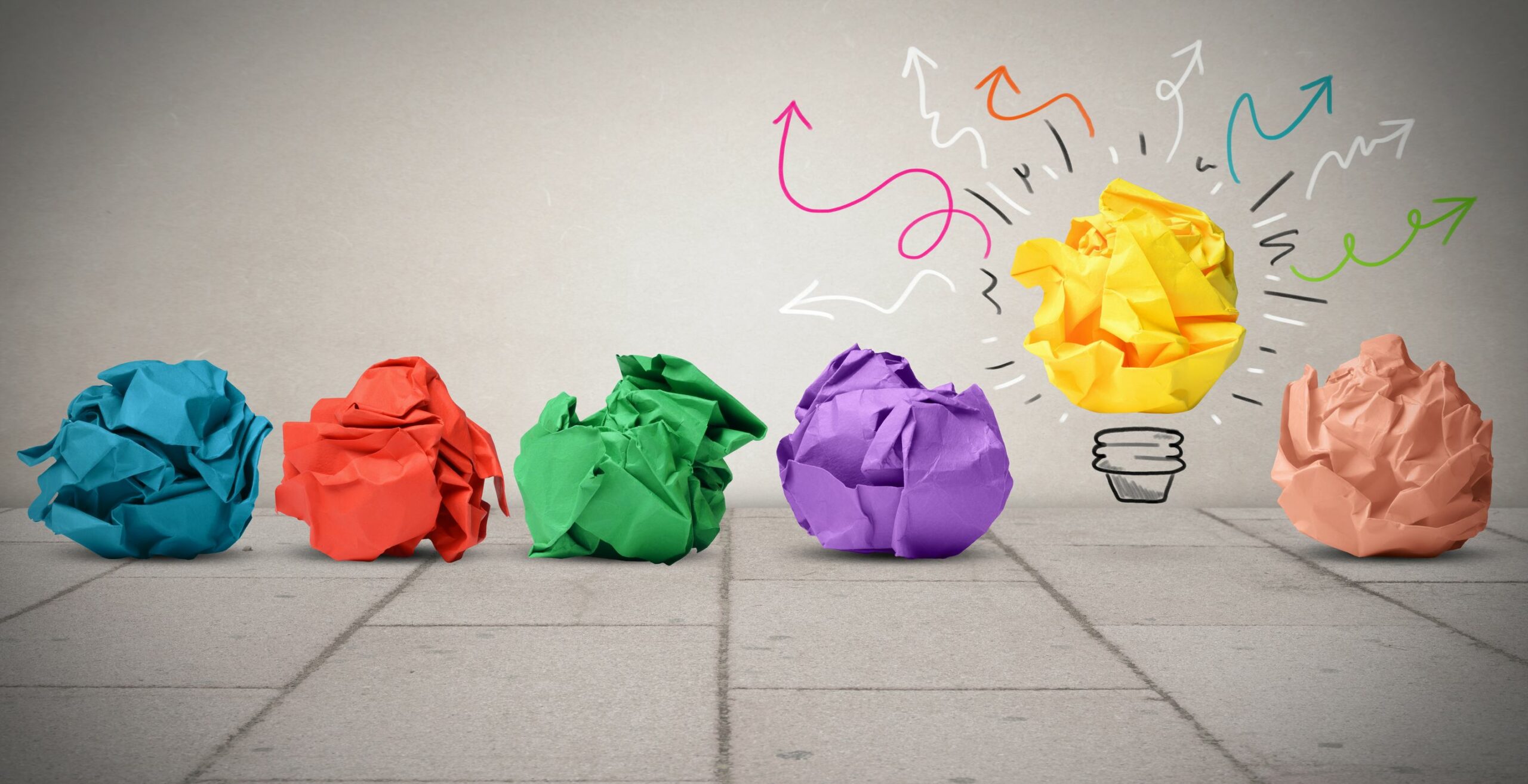 Stock photograph of colourful crumpled balls of paper, with one lighting up like a light bulb with an idea!